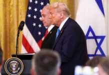 Donald Trump and another official at a press conference with flags in the background