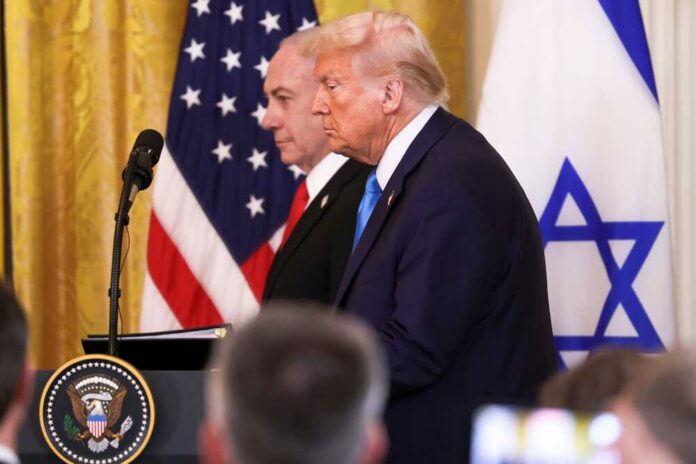 Donald Trump and another official at a press conference with flags in the background