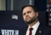 man in suit with red tie at press briefing podium