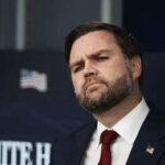 man in suit with red tie at press briefing podium