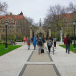 Students walking along a pathway on a university campus with historic buildings in the background