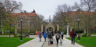 Students walking along a pathway on a university campus with historic buildings in the background