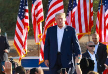 Rushmore Rumble Ignites America’s Identity Fight A speaker at a political rally surrounded by American flags and an engaged crowd