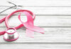 Cancer Surge Warning Rattles WHO A pink ribbon next to a stethoscope on a wooden surface