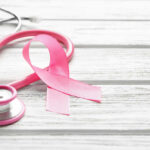 A pink ribbon next to a stethoscope on a wooden surface