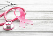 Cancer Surge Warning Rattles WHO A pink ribbon next to a stethoscope on a wooden surface