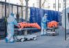 Healthcare workers in PPE move covered stretchers outside a facility