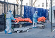 Healthcare workers in PPE move covered stretchers outside a facility