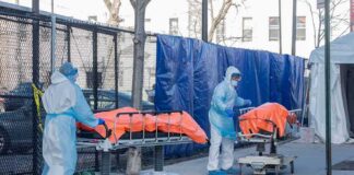 Healthcare workers in PPE move covered stretchers outside a facility