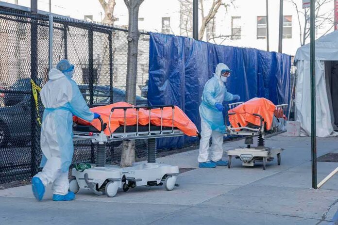 shutterstock_1693764259 Healthcare workers in PPE move covered stretchers outside a facility