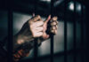 Gen Z Chatroom Labeled Extremist Network Hands gripping prison bars in a dimly lit environment