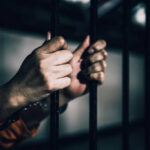 Hands gripping prison bars in a dimly lit environment
