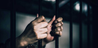 Hands gripping prison bars in a dimly lit environment