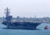 Aircraft carrier escorted by a tugboat in a harbor