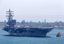 Gulf Showdown Escalates — Twelve Nights And Counting Aircraft carrier escorted by a tugboat in a harbor