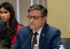 DSA Bombshell Claims Ignite Firestorm man in a blue suit speaking into a microphone at a meeting