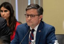 DSA Bombshell Claims Ignite Firestorm man in a blue suit speaking into a microphone at a meeting