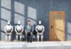 Dutch Hub Quietly Arms The Robots A man sitting between three humanoid robots in a waiting room for a job interview
