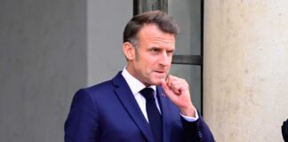 Emmanuel Macron in a suit, standing outdoors with a thoughtful expression