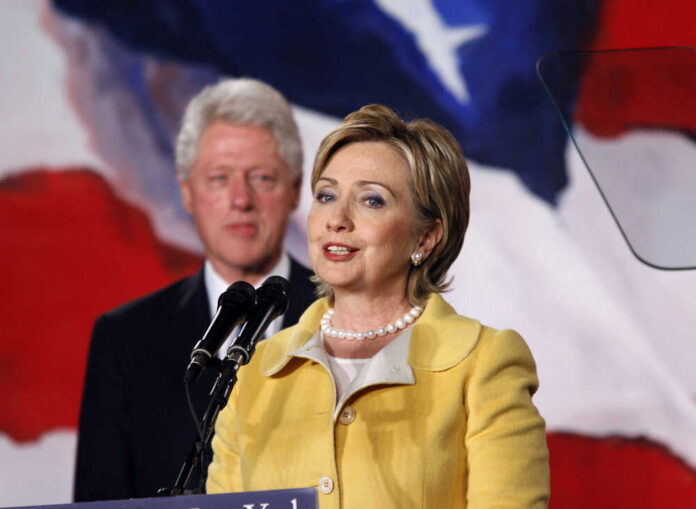 Bill,And,Hilary,Clinton Hillary Clinton speaking at a podium with Bill Clinton in the background