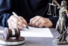 Gunpoint Raid Sparks Seven-Figure Payout Judge writing at desk with gavel and Lady Justice statue