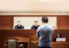 defendant stands before judges in a courtroom