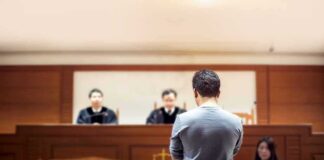 defendant stands before judges in a courtroom