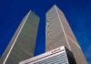 Twin rectangular skyscrapers rising above a hotel facade against a clear blue sky