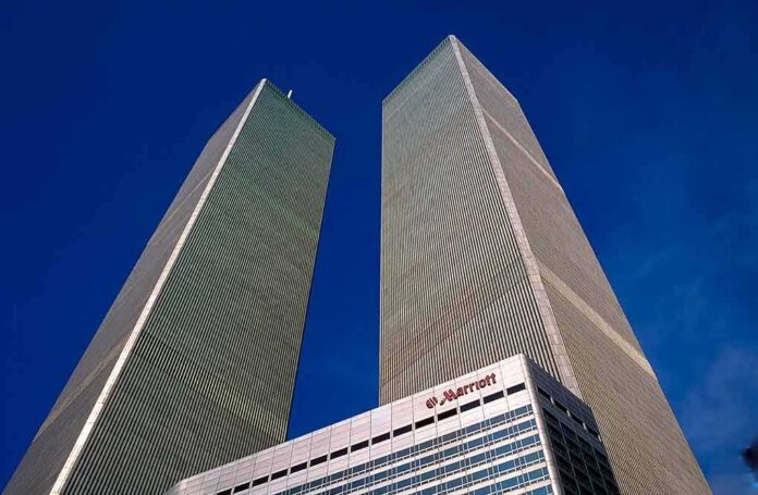 shutterstock_1095776192 Twin rectangular skyscrapers rising above a hotel facade against a clear blue sky