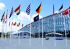 Putin Probe Rumors—Trump Brushes Off Danger Row of national flags outside a modern glass building