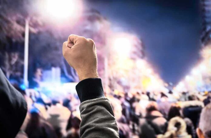 shutterstock_1227767953 Raised fist in front of a large crowd at night