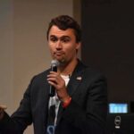 Political Hit Claim Sparks Capital Fight man speaking into a microphone on stage