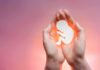 hands cupping a fetal silhouette on pink background