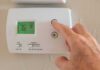 Hand adjusting a digital thermostat on a wall