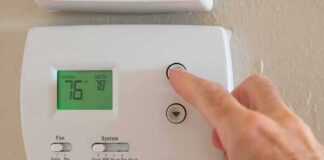 Hand adjusting a digital thermostat on a wall