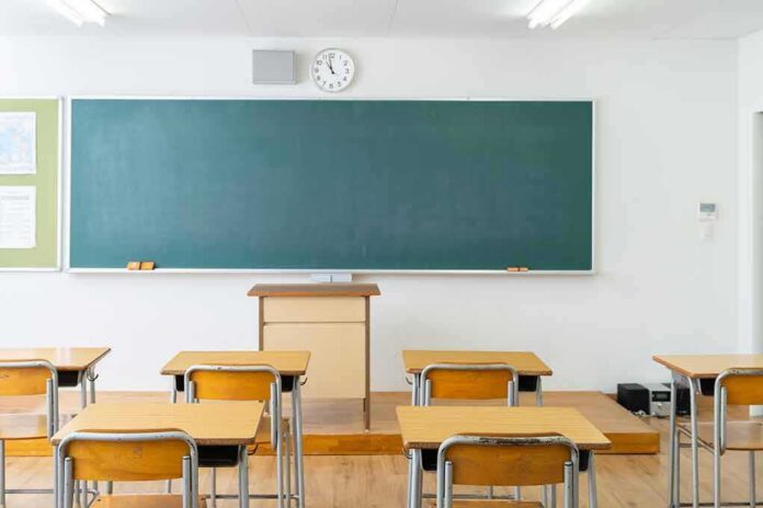 shutterstock_1940009296 Empty classroom with desks facing a large chalkboard