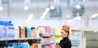 Woman shopping in a supermarket aisle with a red basket