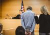 Defendant in handcuffs stands before a judge in a courtroom