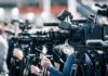 Legal Showdown Looms Over Child-Care Cash Broadcast cameras on tripods at a press event