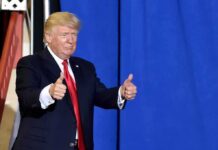 Donald Trump giving two thumbs up in front of a blue curtain