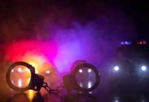 Gas Pump Showdown Stuns Suburb Handcuffs on a surface with police cars and flashing lights in smoky darkness