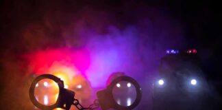 Handcuffs on a surface with police cars and flashing lights in smoky darkness
