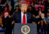 Donald Trump speaking at a rally podium with arms raised