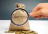 Arab Bloc Endorses UK Sanctions Blitz hand holding magnifying glass over burlap money bag with coins