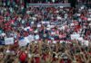 Speaker at podium addresses large crowd at indoor political rally