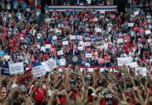 Speaker at podium addresses large crowd at indoor political rally