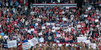 Speaker at podium addresses large crowd at indoor political rally