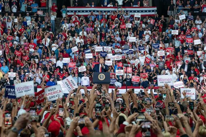 shutterstock_1480255829 Speaker at podium addresses large crowd at indoor political rally