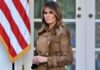 Melania Trump standing in a brown suede coat near an American flag