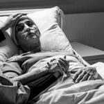 Patient in hospital bed with nasal oxygen held by visitor